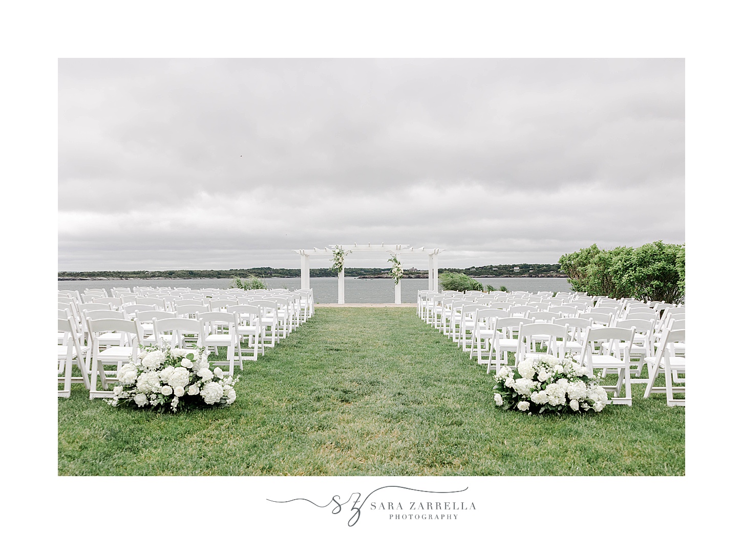 ceremony along water on lawn at OceanCliff Hotel with white arbor and white flowers 