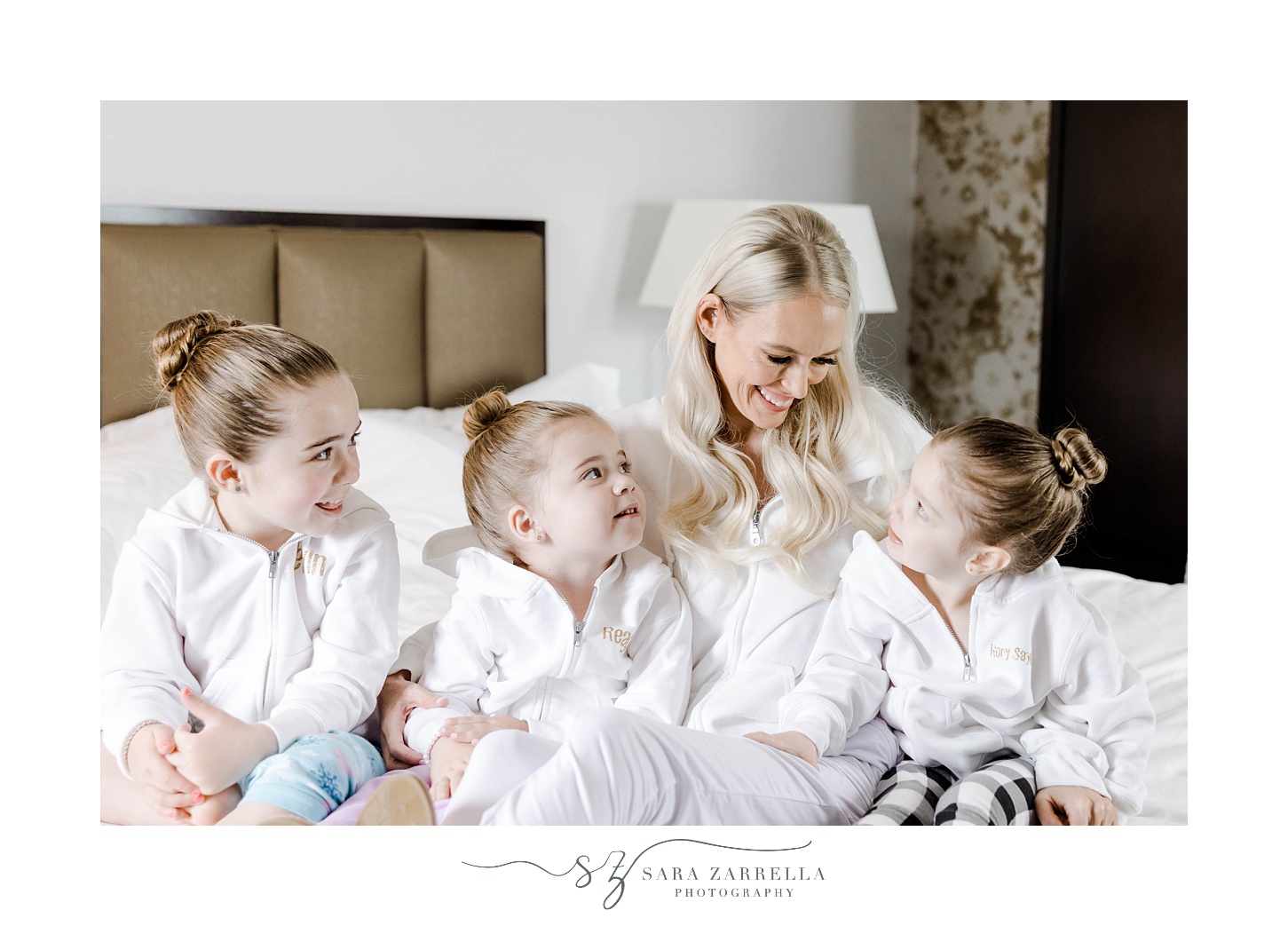 bride laughs with flower girls sitting on bed