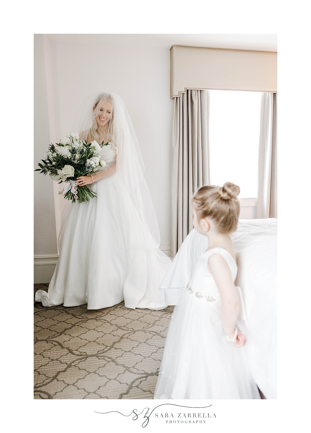 bride holds bouquet and looks at flower girl in hotel room at Omni Providence Hotel
