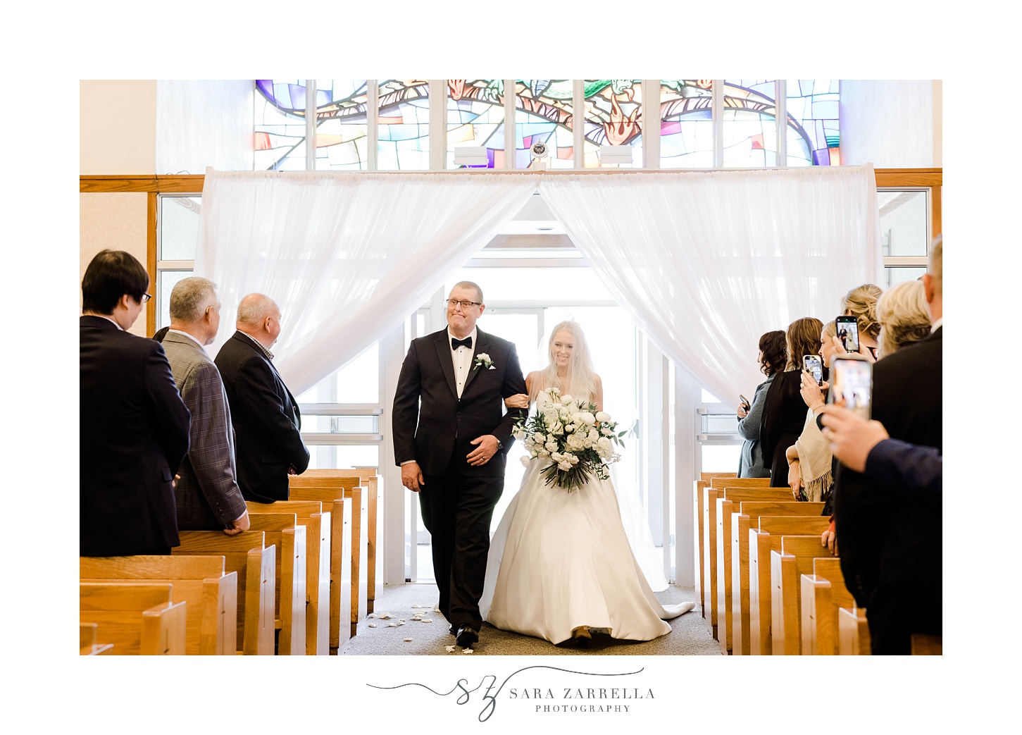 bride and father walk down aisle during  wedding ceremony at St. Michael’s Parish in Smithfield