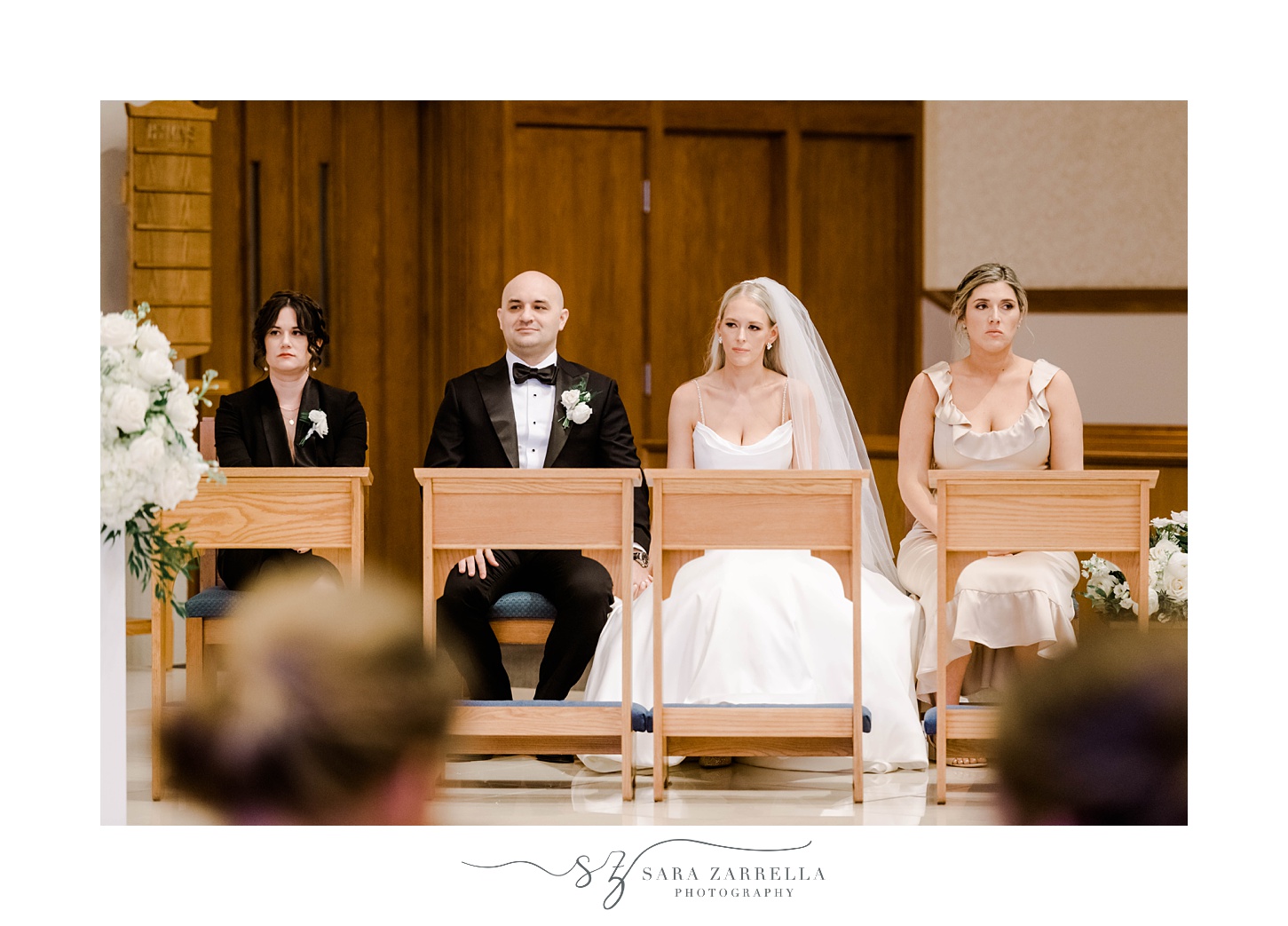 bride and groom sit with bridesmaid and best woman during wedding ceremony at St. Michael’s Parish in Smithfield