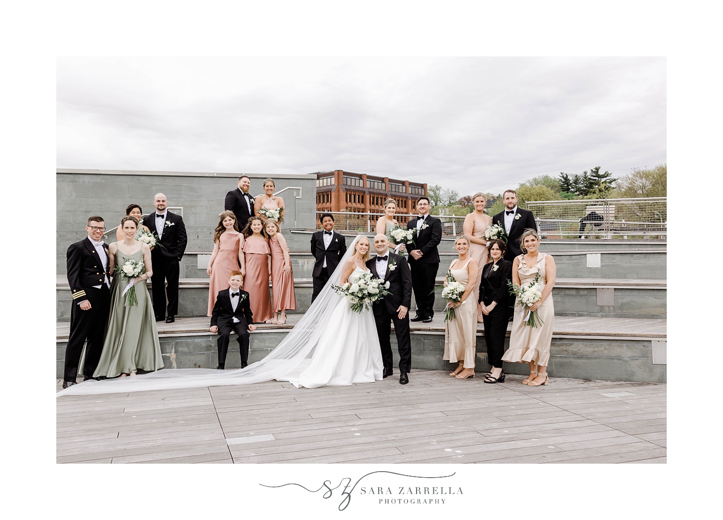 newlyweds stand on Providence pedestrian bridge with wedding party in pink, green, and black