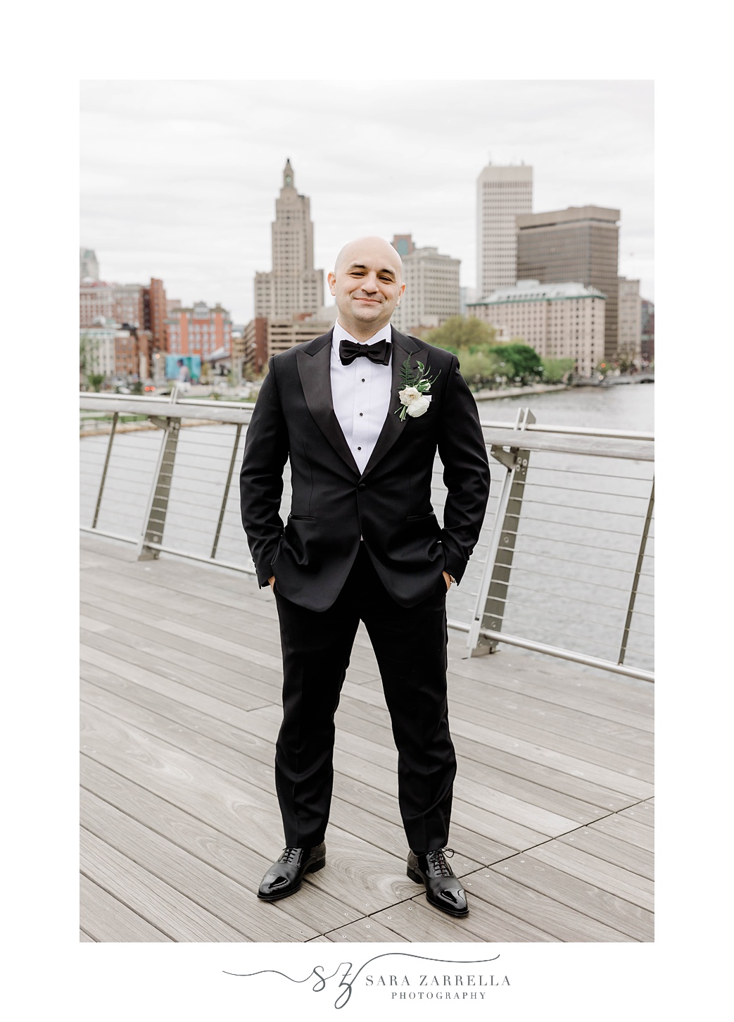 groom stands on the Providence pedestrian bridge with hands in pockets