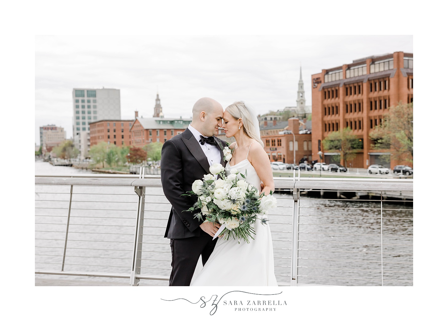 newlyweds lean heads together against railing at the Providence pedestrian bridge
