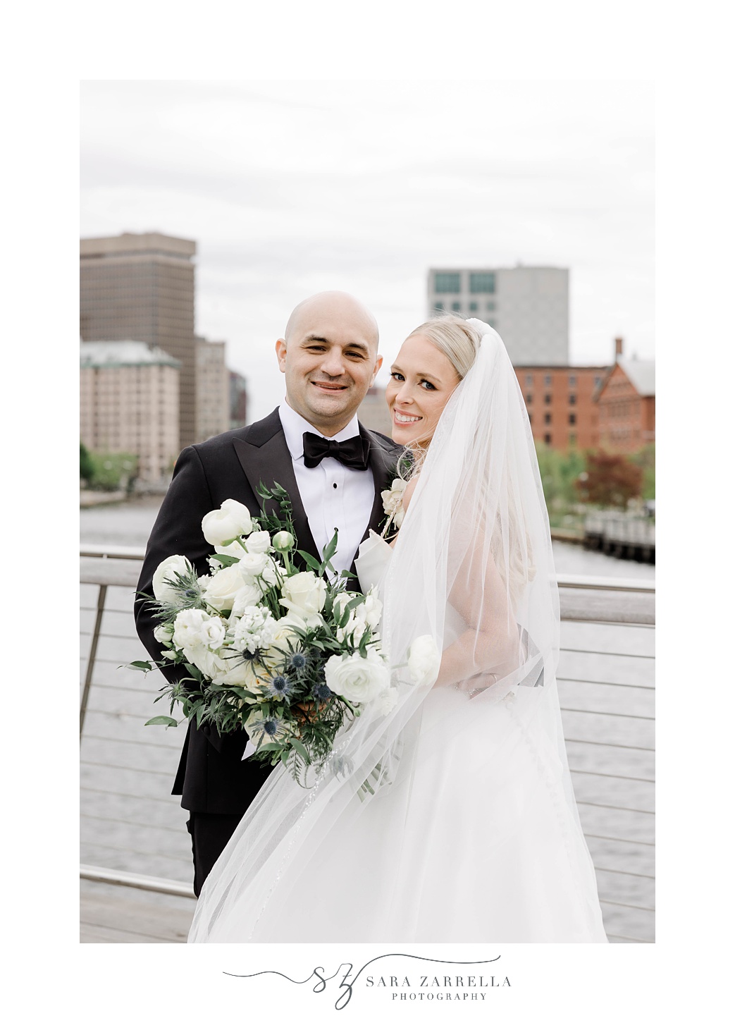 bride and groom hug on waterfront at Providence pedestrian bridge