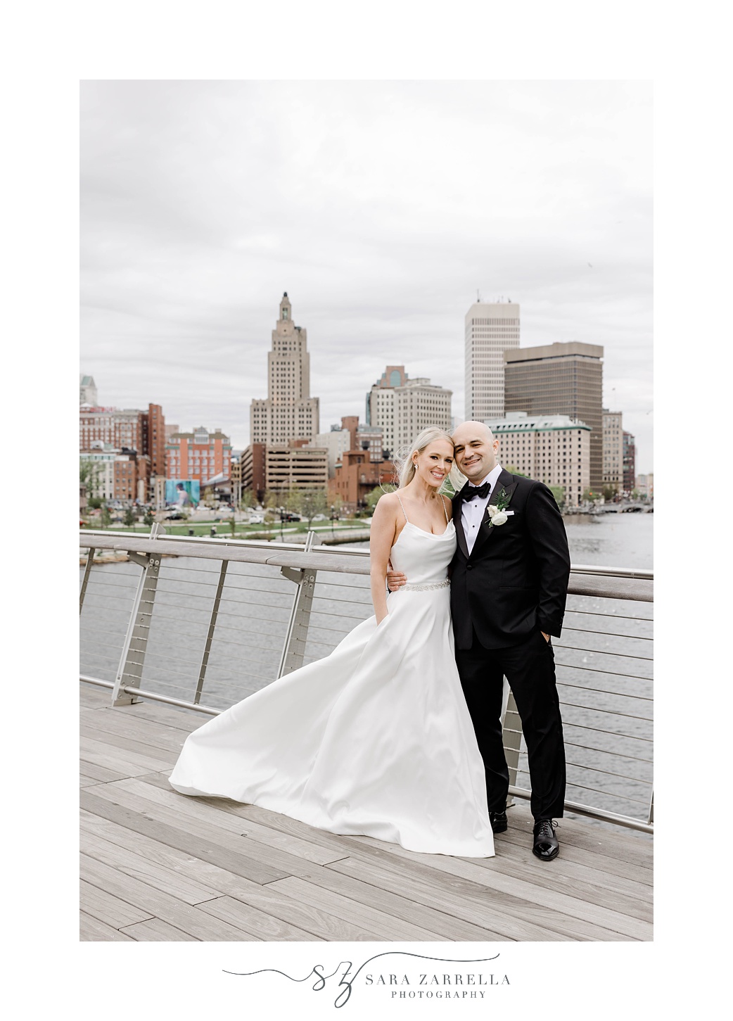 newlyweds stand on Providence pedestrian bridge with Rhode Island skyline behind them