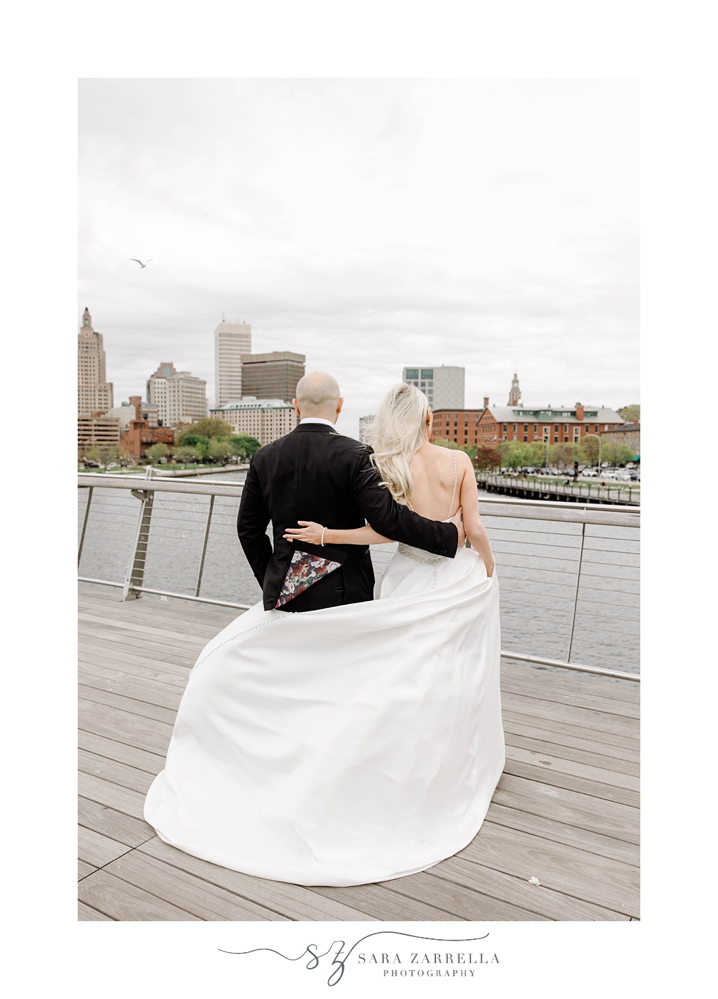 newlyweds stand on the Providence pedestrian bridge looking at water 