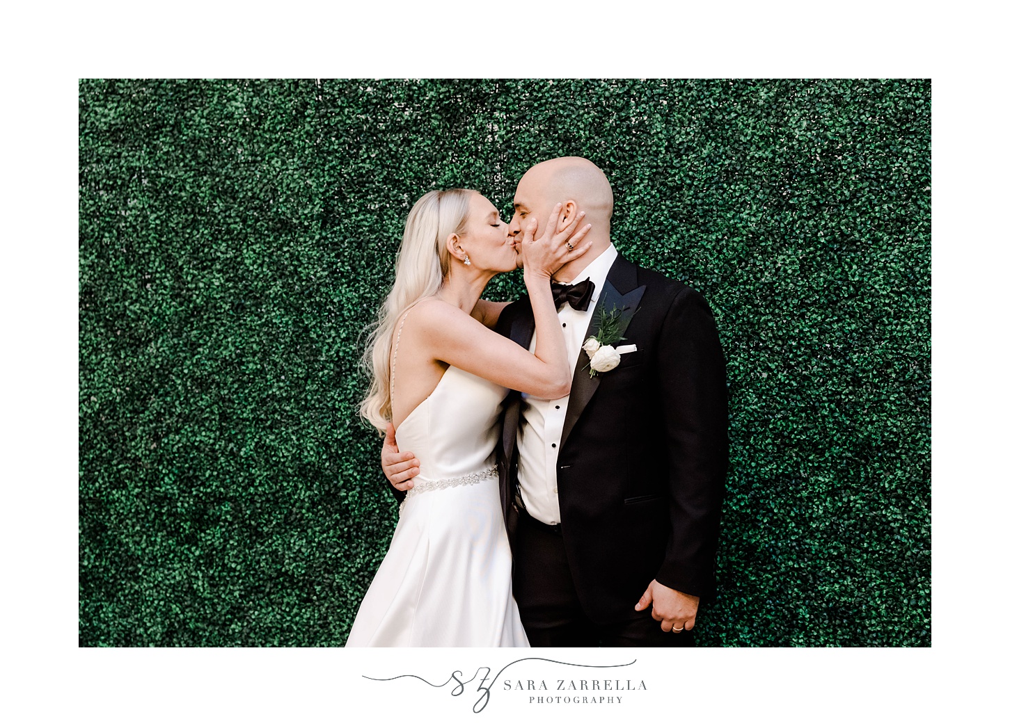 newlyweds kiss by greenery wall of photo booth