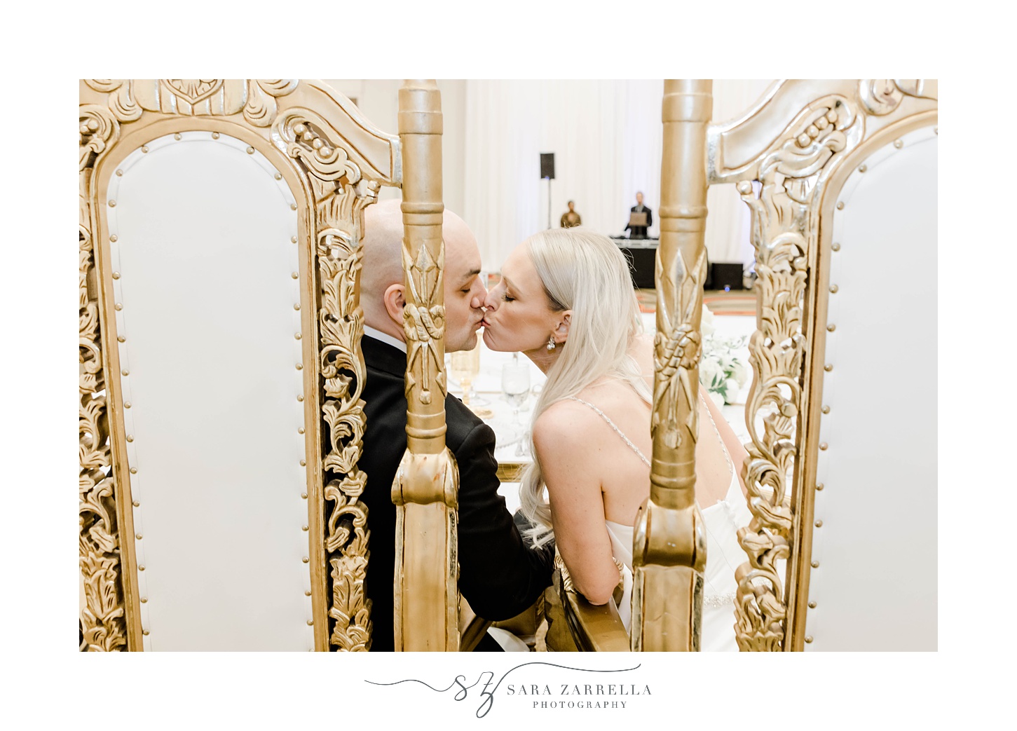 newlyweds kiss in gold chairs during Omni Providence Hotel wedding reception