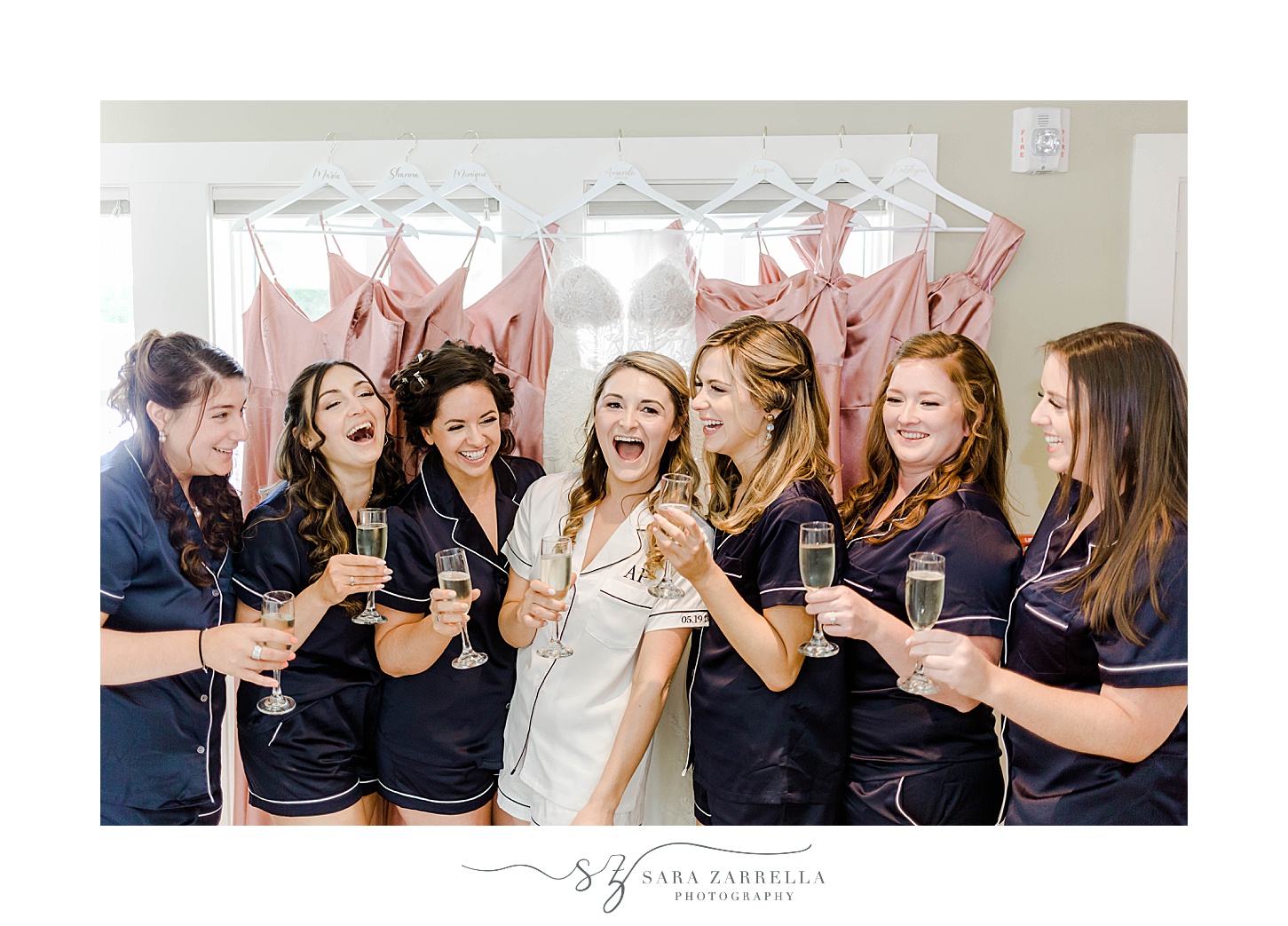 bride laughs with bridesmaids in matching pajamas in front of pink gowns in window at Wequassett Resort