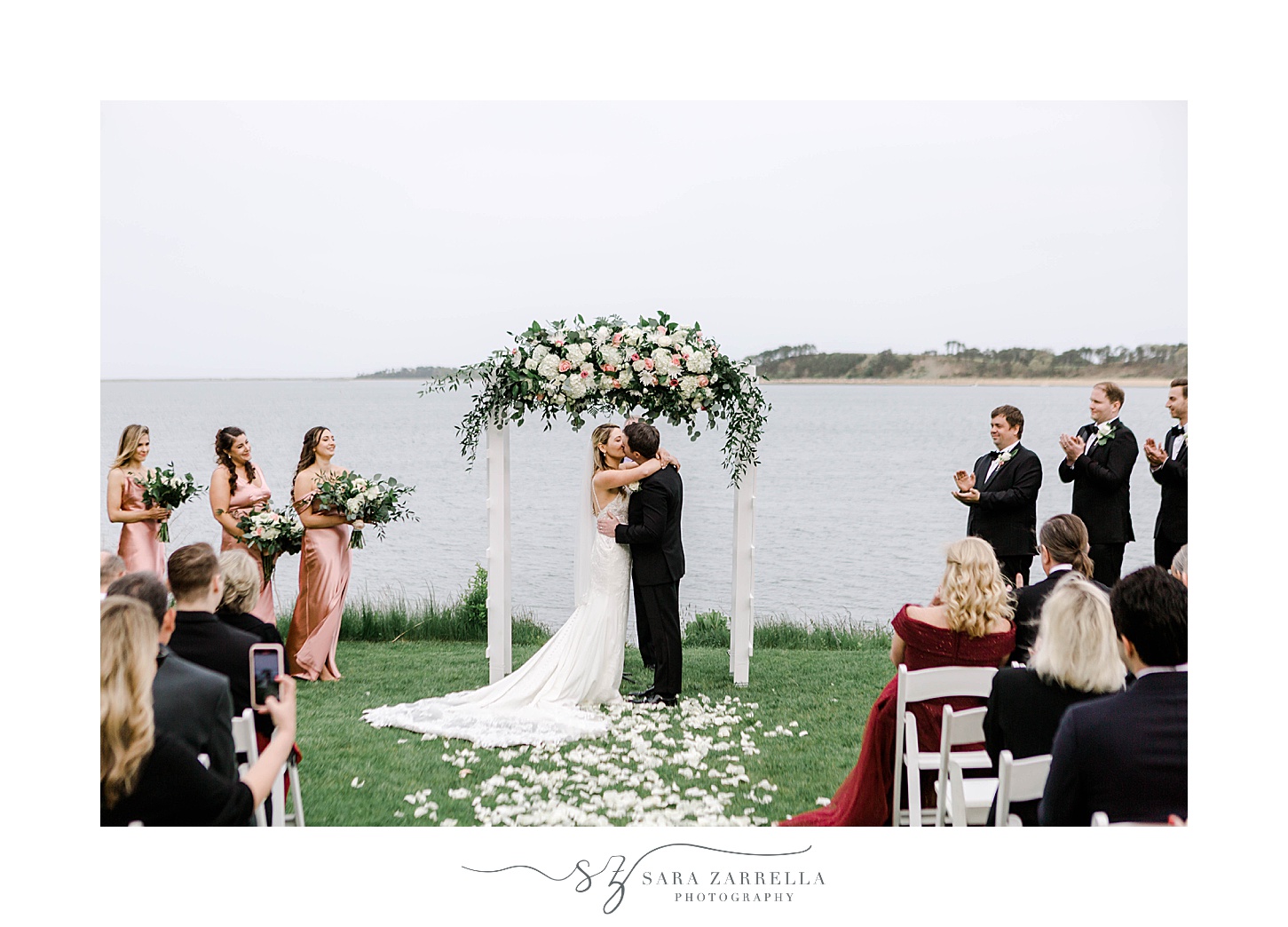bride and groom hug and kiss under floral arbor at Wequassett Resort