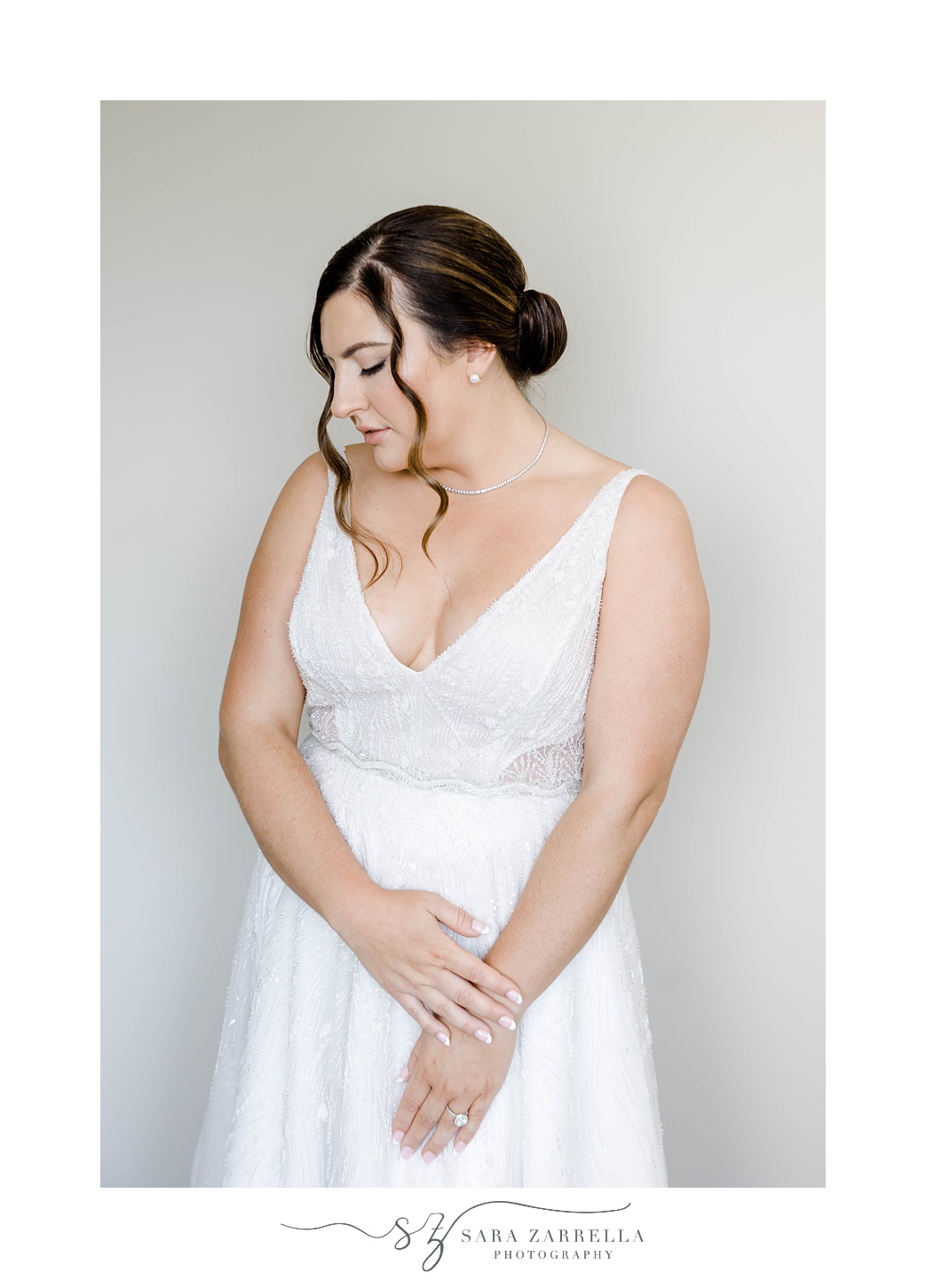 bride stands holding wrist looking over shoulder in dress with v-neck