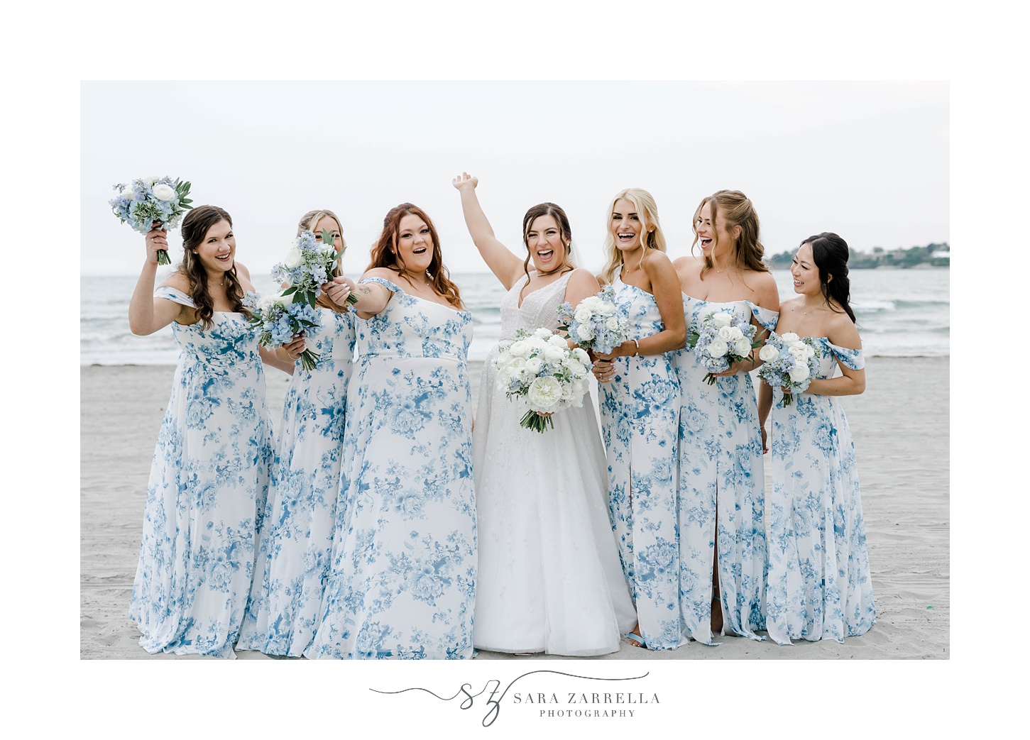 bride and bridesmaids in blue and white gowns cheer on beach