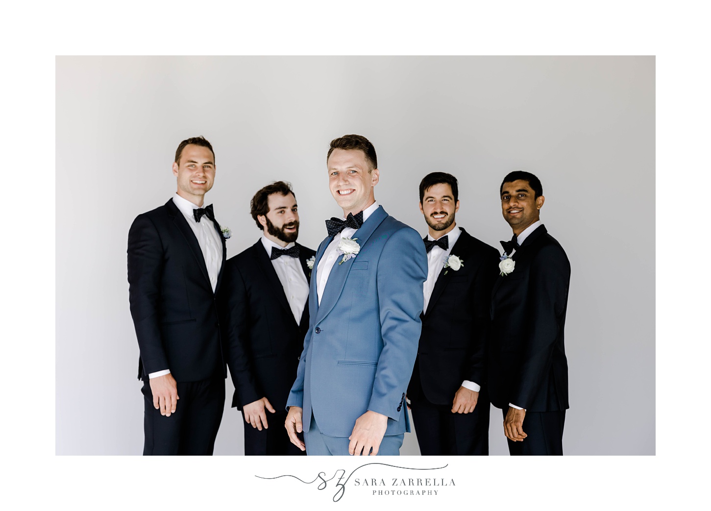 groom stands with groomsmen in front of white wall at Newport Beach House