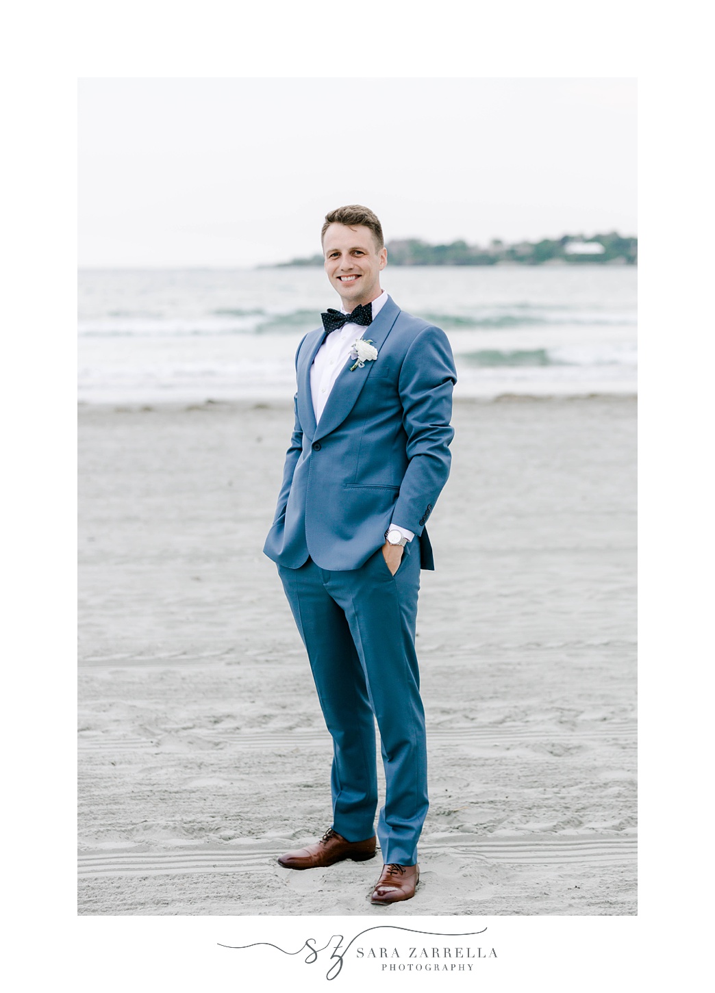 groom stands in blue suit on Newport Beach