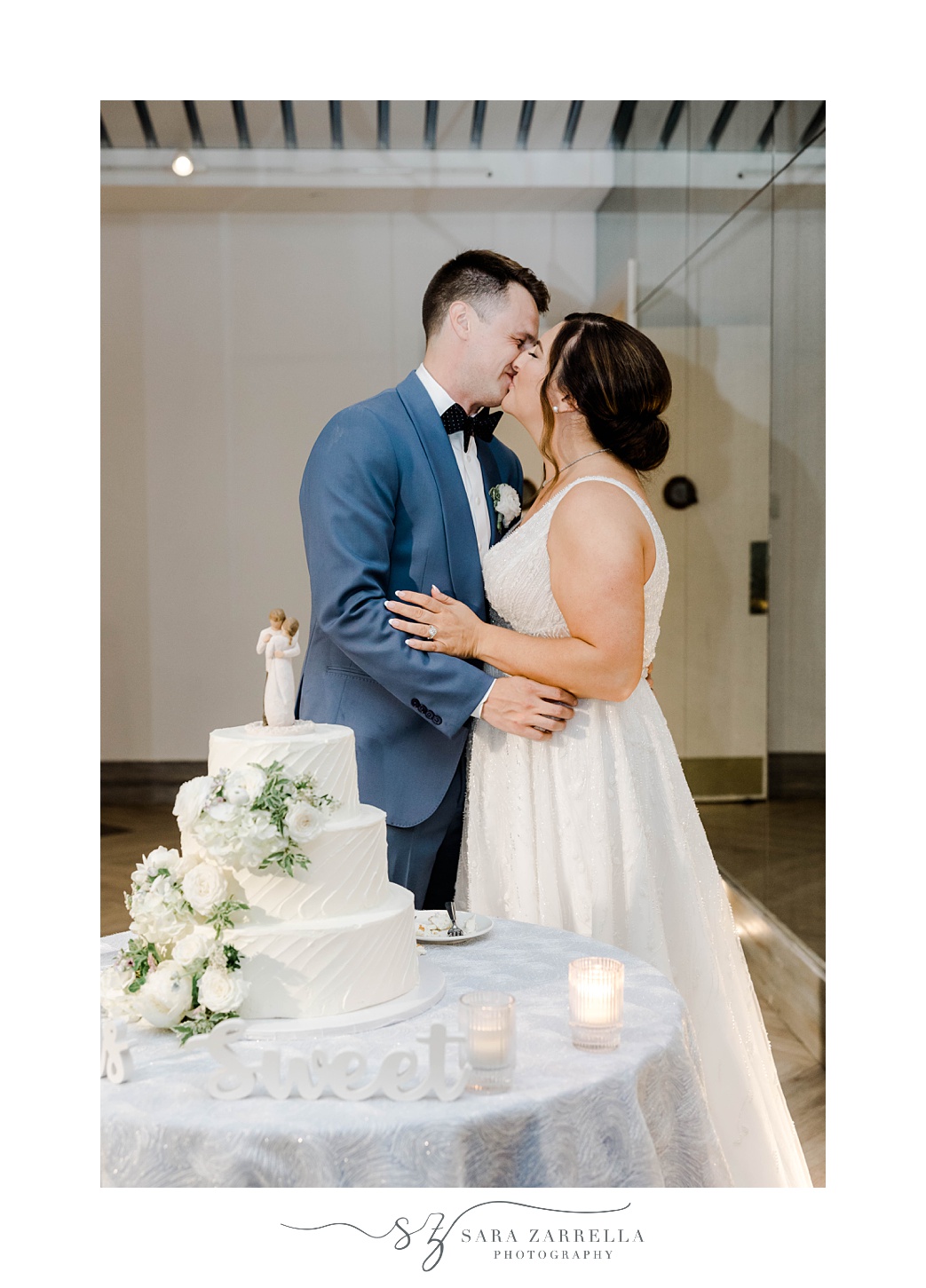 newlyweds kiss by tiered wedding cake during Newport RI wedding reception
