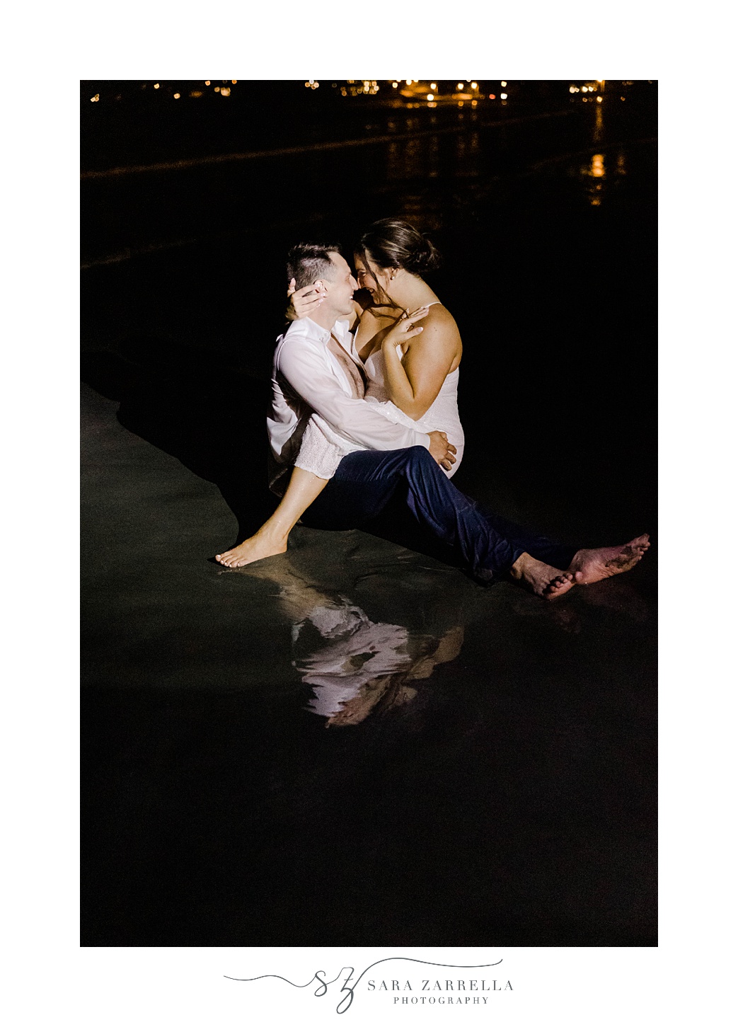 bride sits on groom's lap leaning to kiss him on the beach at night