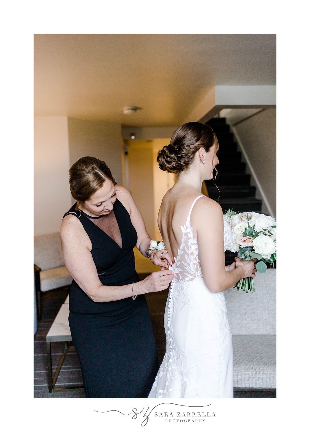 bridesmaid helps bride into wedding dress in suite at OceanCliff Hotel