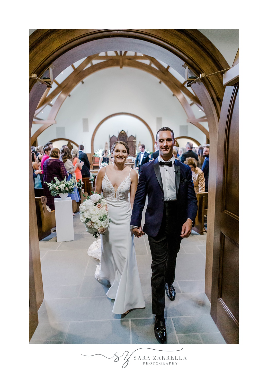 groom holds bride's hand leaving wedding ceremony at Our Lady of Mercy Chapel at Salve Regina University