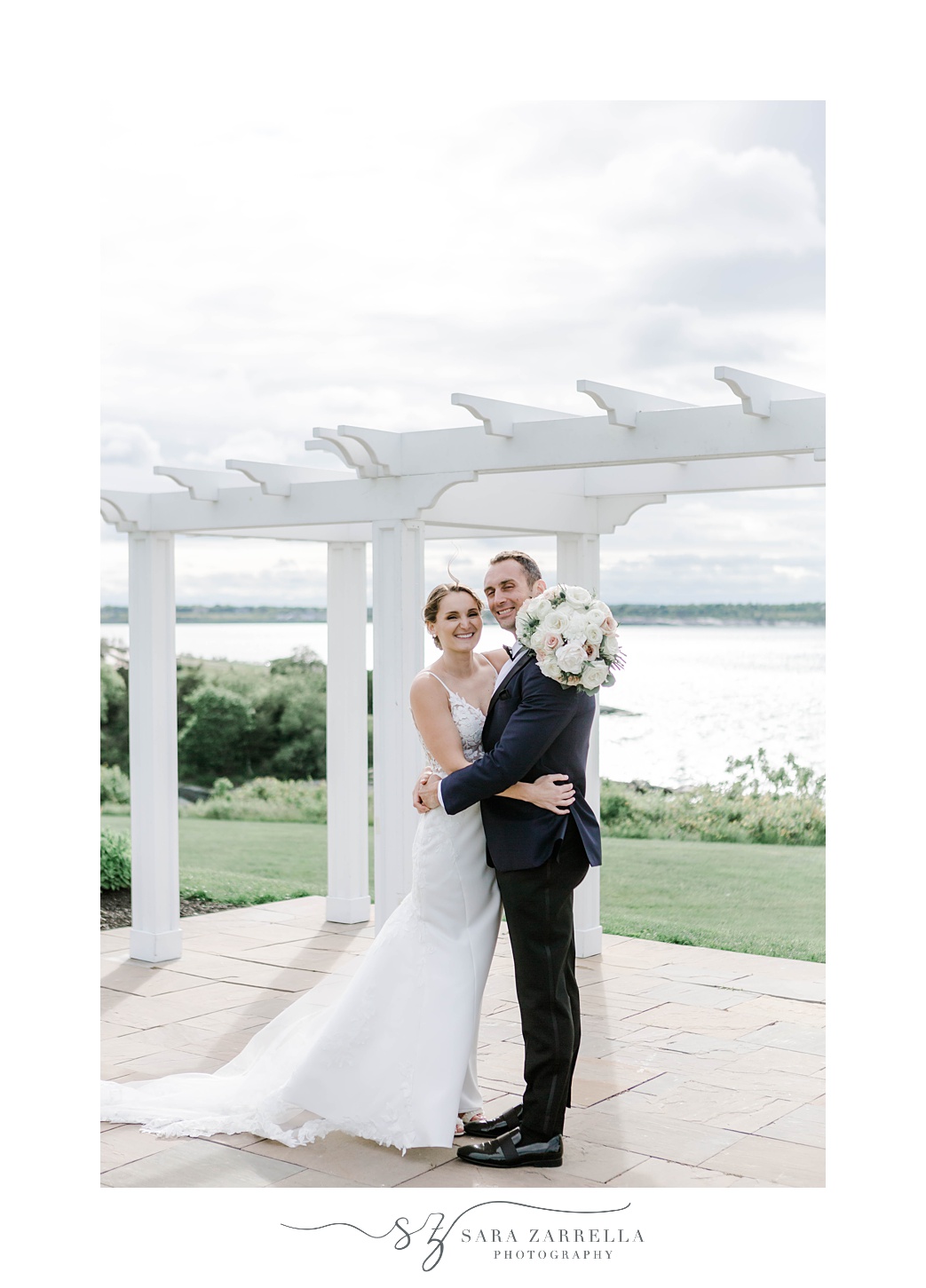 newlyweds hug during portraits at OceanCliff Hotel in front of white arbor