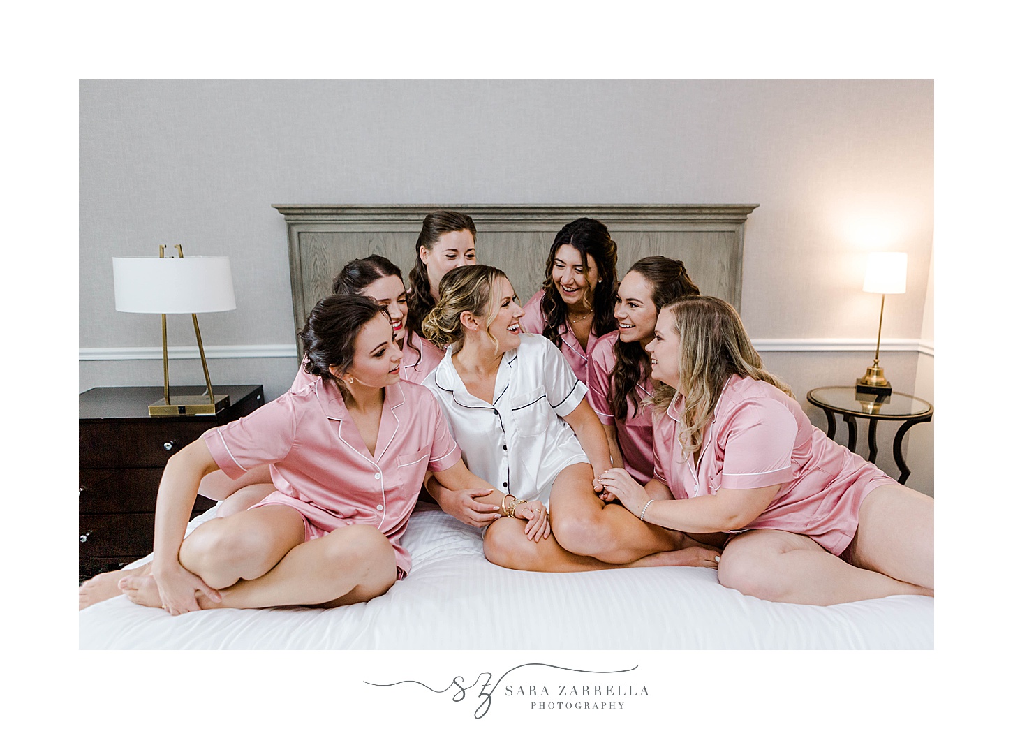 bride sits on bed with bridesmaids in pink and white robes