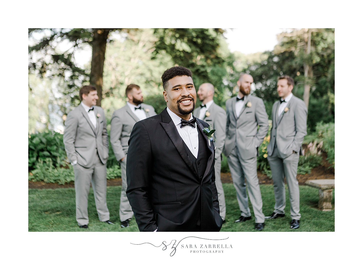 groom stands in front of groomsmen in grey suits on lawn at Glen Manor House