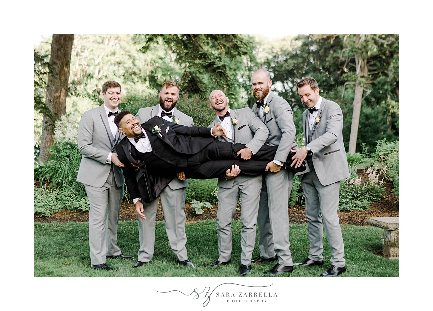 groomsmen in grey suits hold up groom on lawn at Glen Manor House