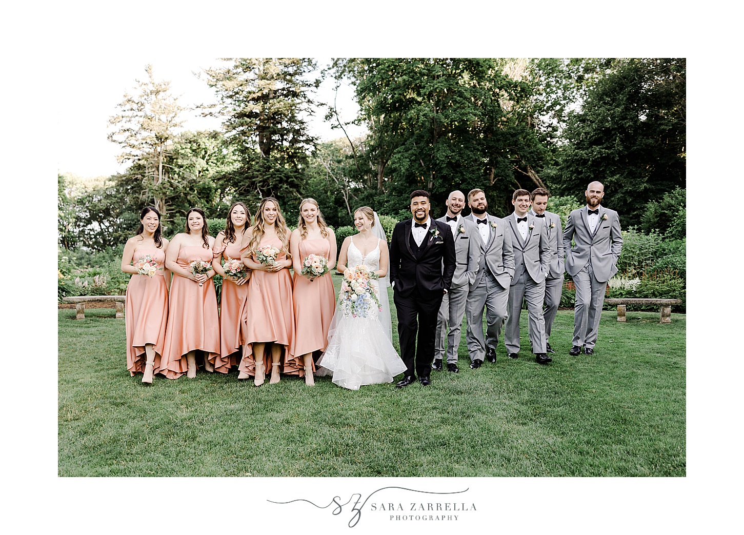 bride and groom walk with wedding party in grey suits and coral dresses 