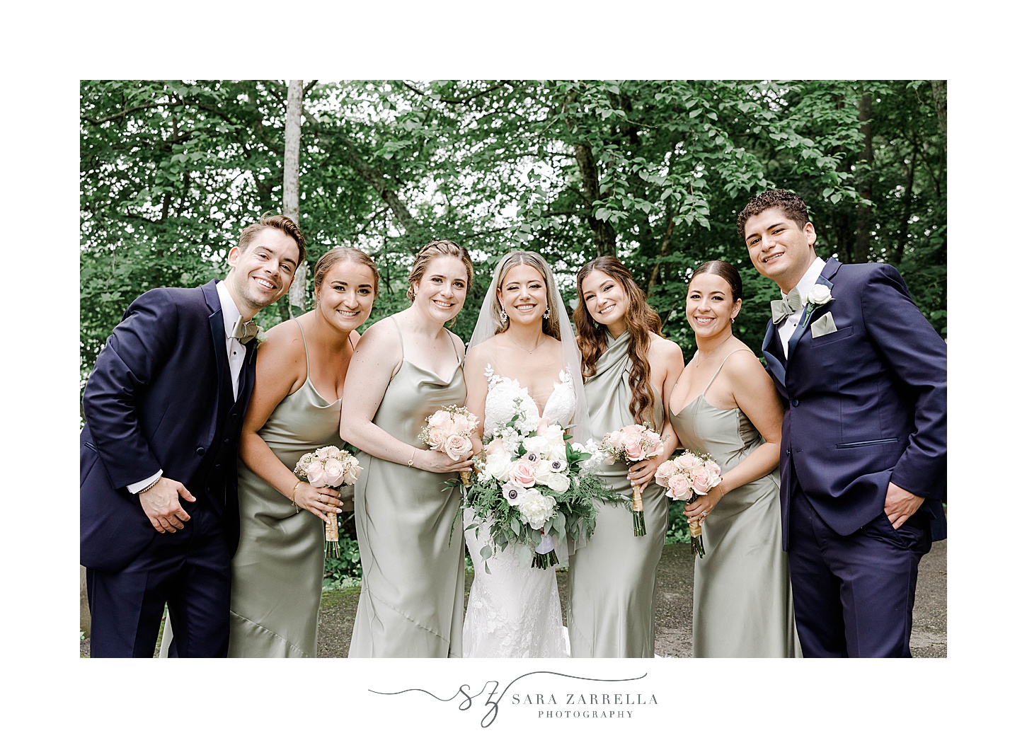 bride poses with bridesmaids in green gowns and men in navy suits 