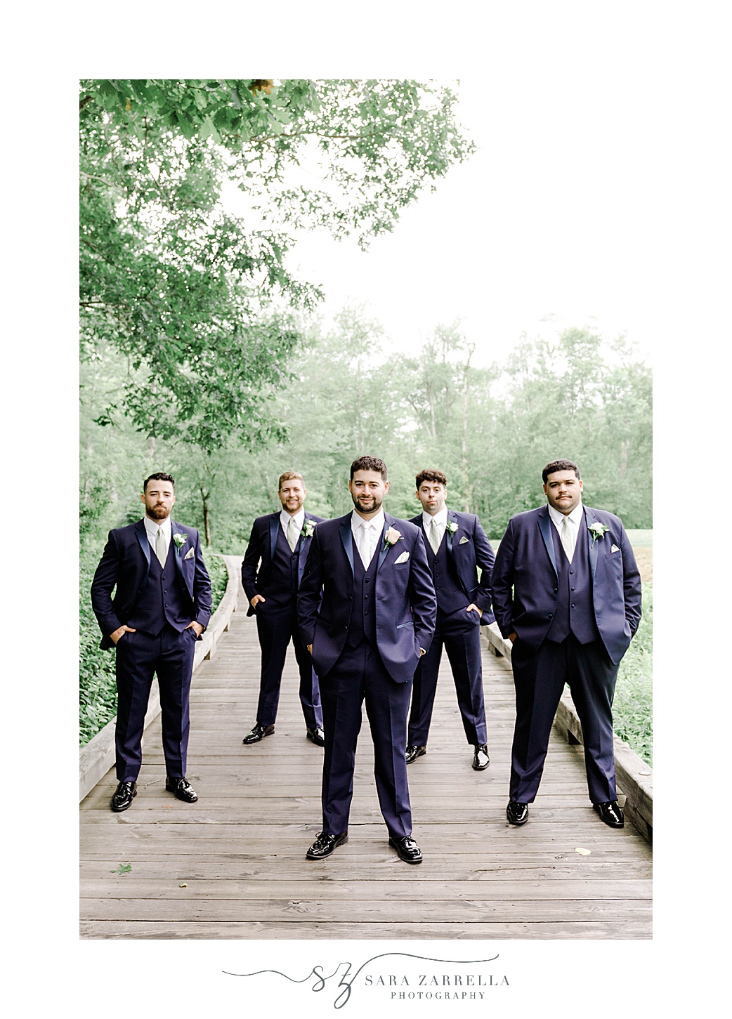 groom and groomsmen stand on dock scattered at the Lake of Isles