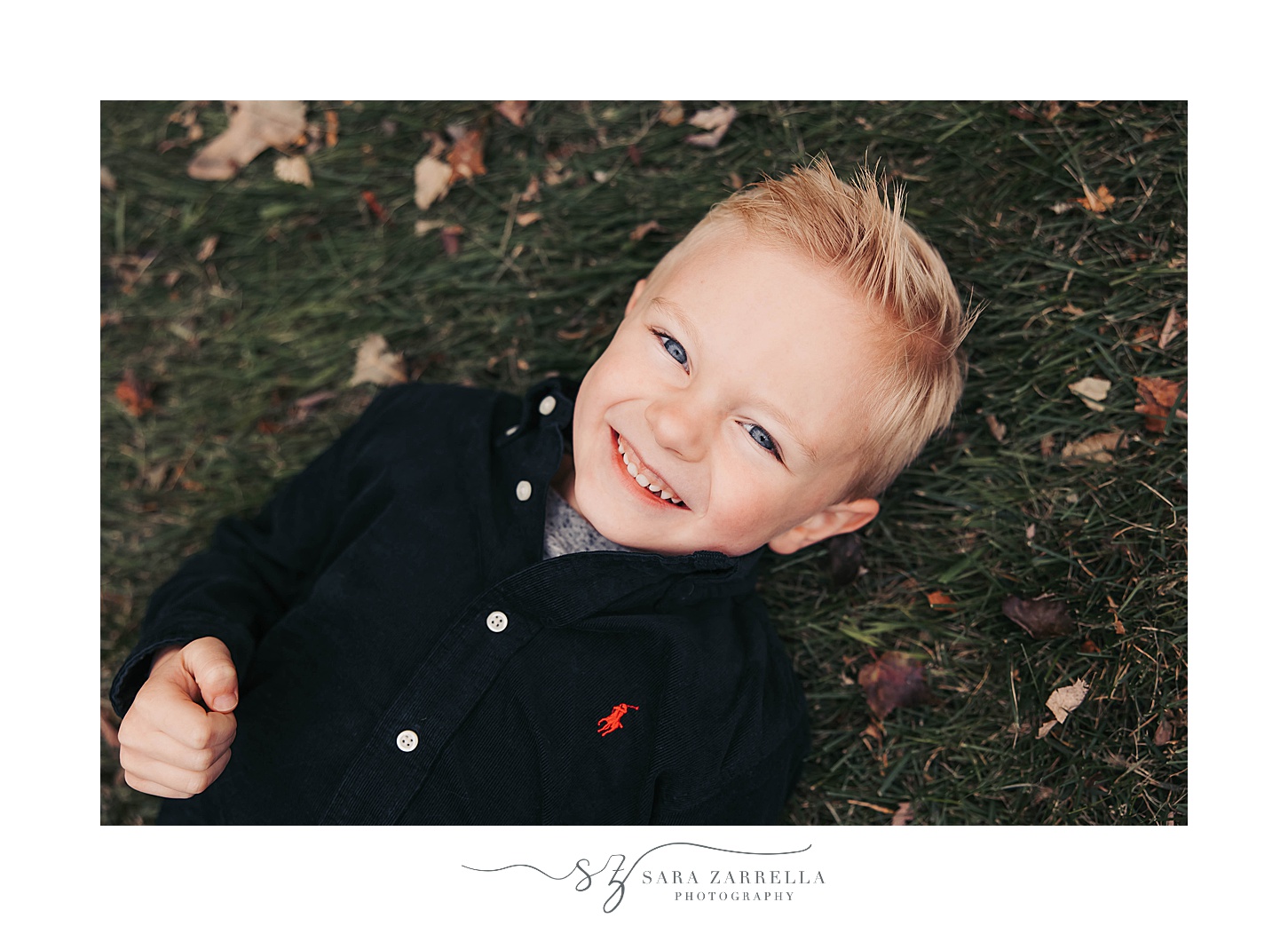 blonde boy lays on ground with leaves around his head during fall mini session