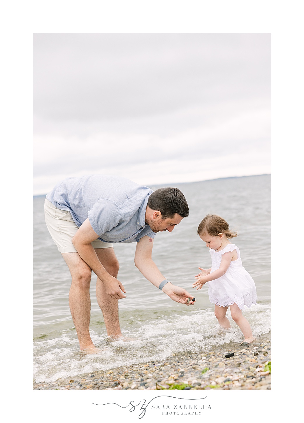 dad leans down to give toddler daughter shell during Beach mini sessions
