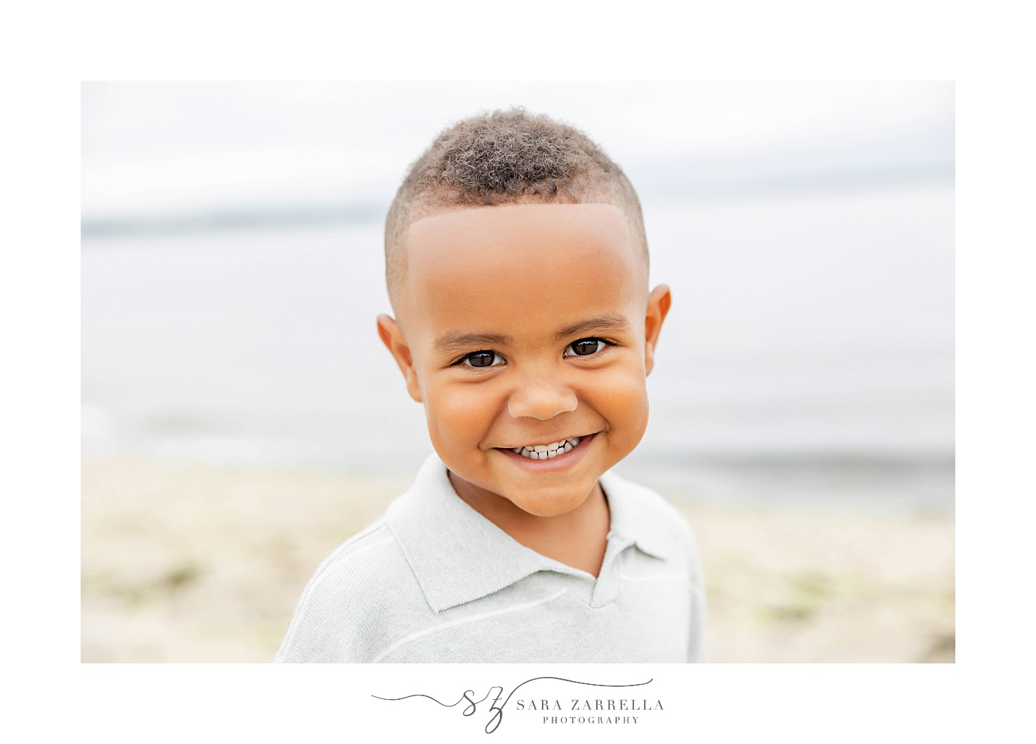 toddler grins at camera in pale blue polo on beach