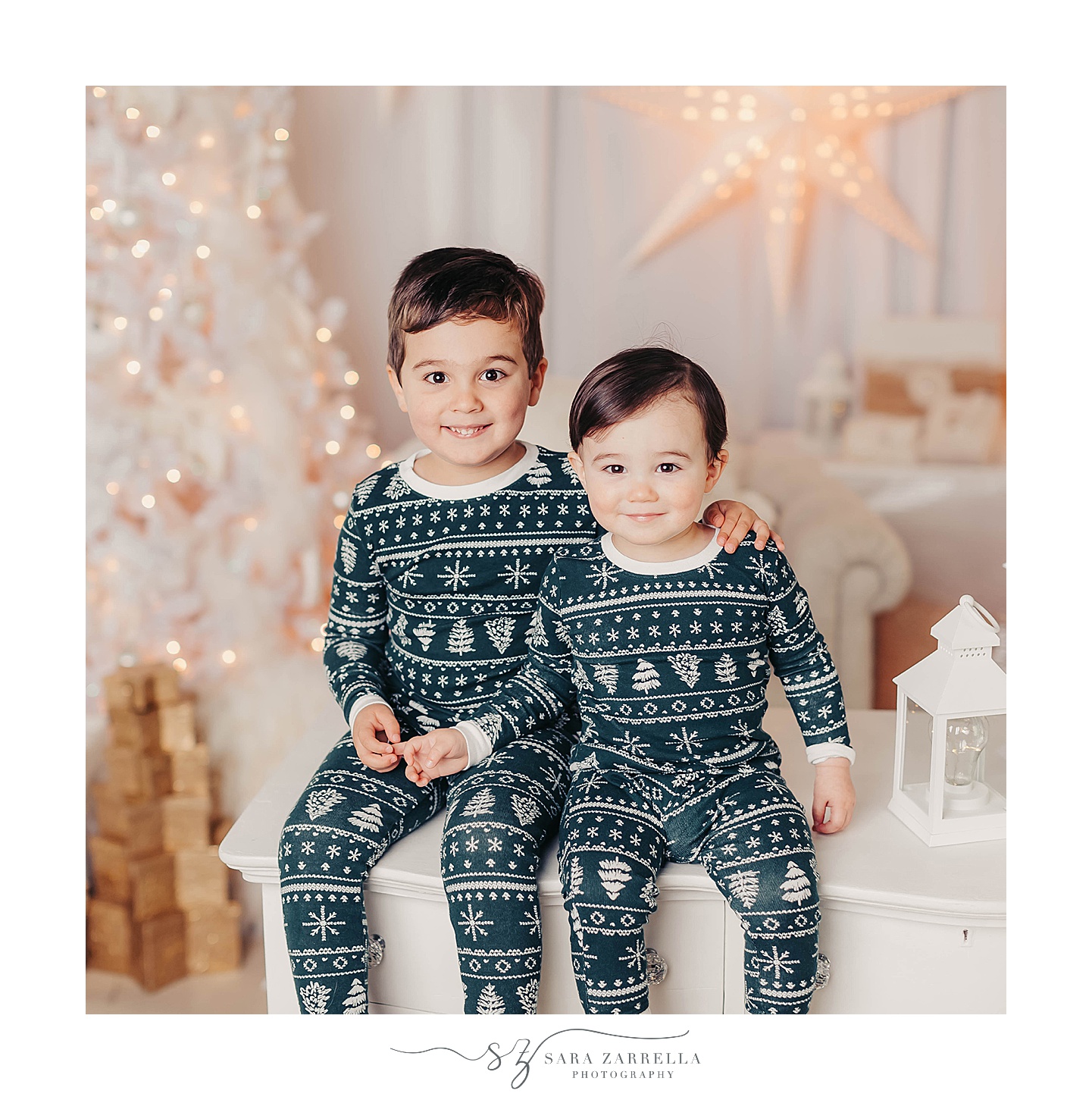 bothers in matching Christmas pajamas sit on white table