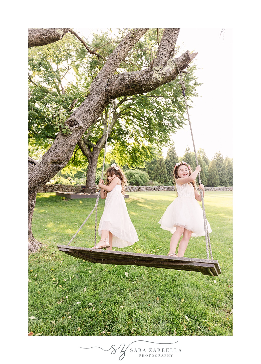 sisters swing on wooden swing during summer mini session on farm in Rhode Island