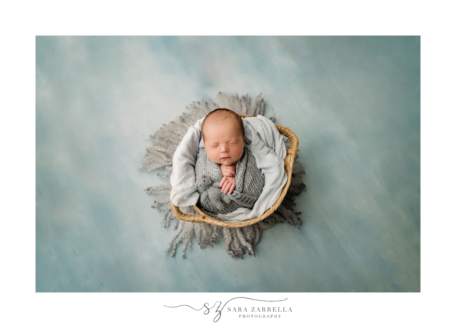 baby boy sleeps in basket with white and grey linens in newborn session in Rhode Island