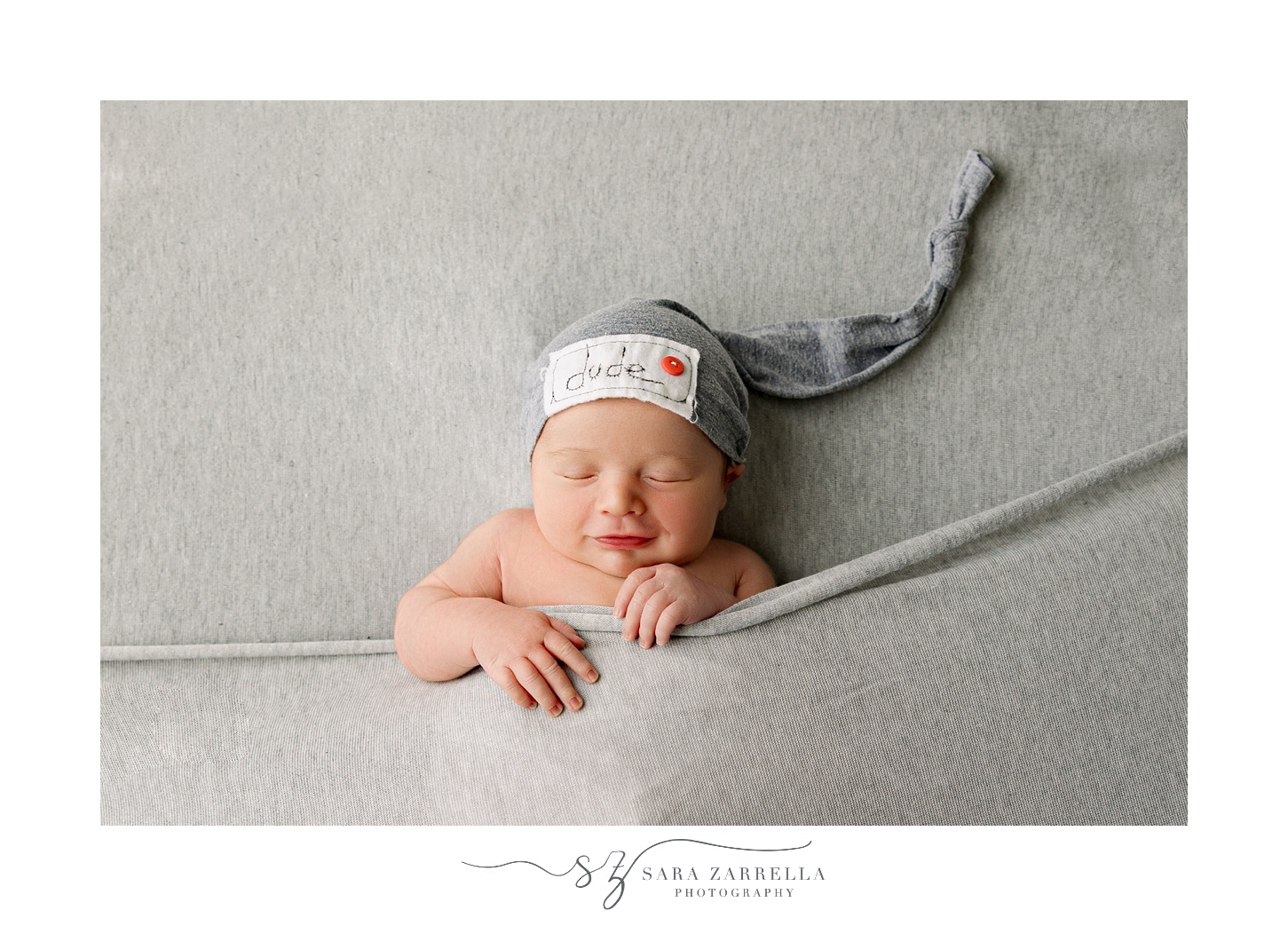 baby lays under grey blanket wearing blue hat during newborn session with Rhode Island newborn and family photographer Sara Zarrella Photography