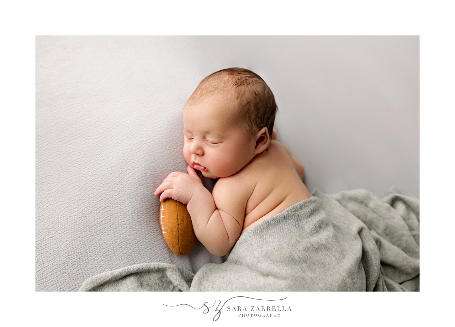 baby sleeps holding football during newborn session with Rhode Island newborn and family photographer Sara Zarrella Photography