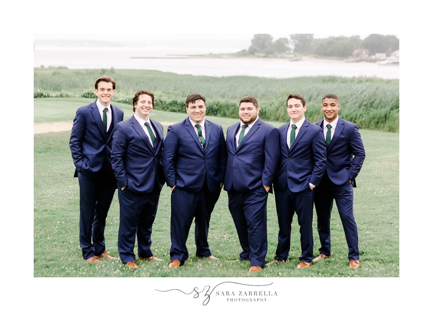 groom stands with groomsmen in navy suits on hill at Harbor Lights