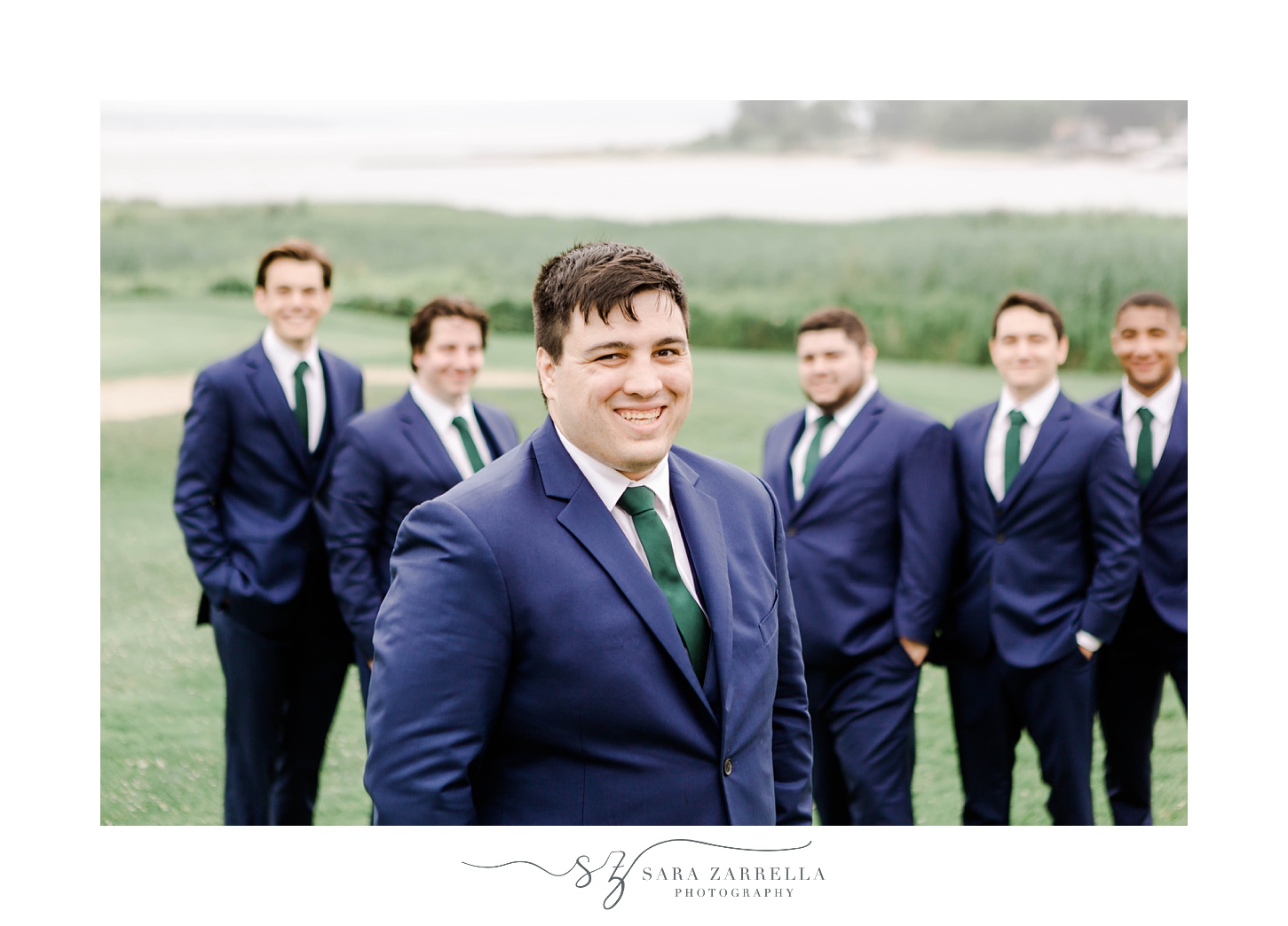 groom stands in navy suit with green tie with groomsmen during Warwick RI wedding day