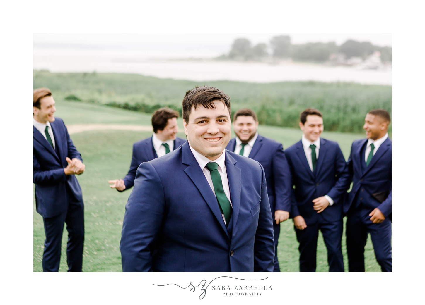 groom and groomsmen stand together on hill talking at Harbor Lights