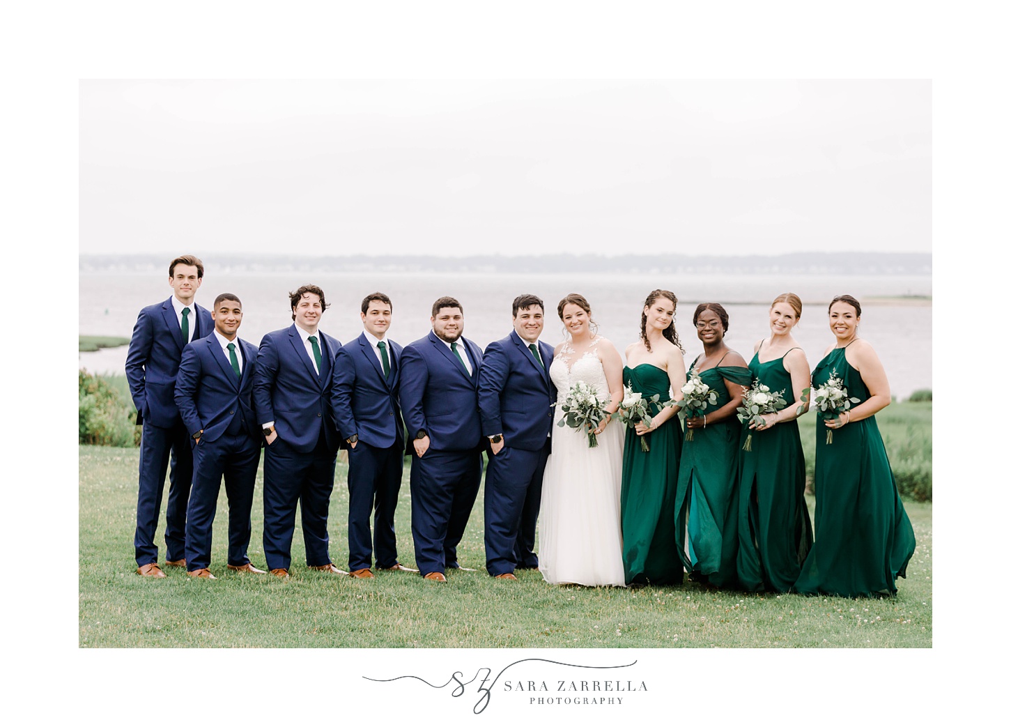 bride and from pose with wedding party in navy suits and green gowns on hill at Harbor Lights