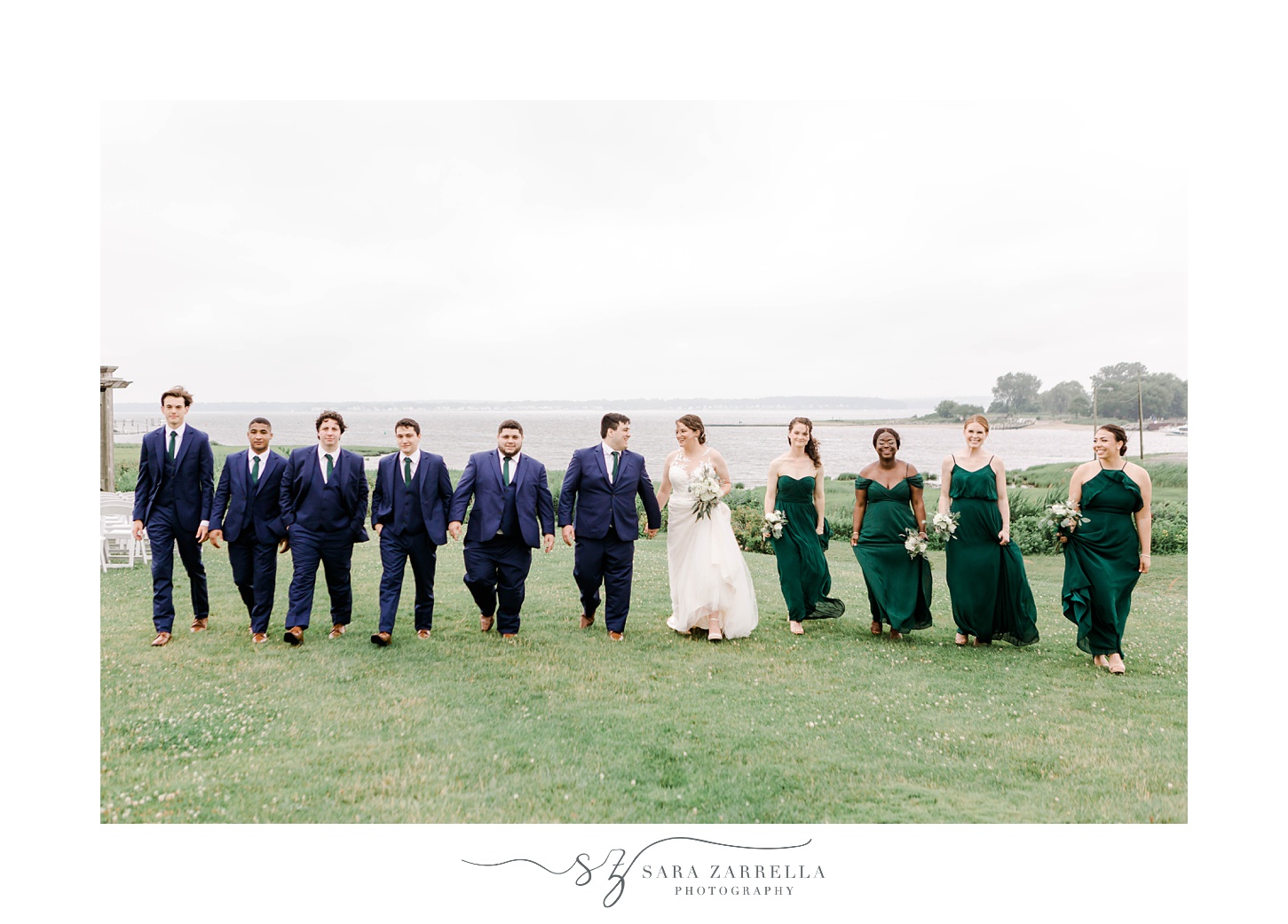 bride and groom walk with wedding party on hill in front of Narragansett Bay