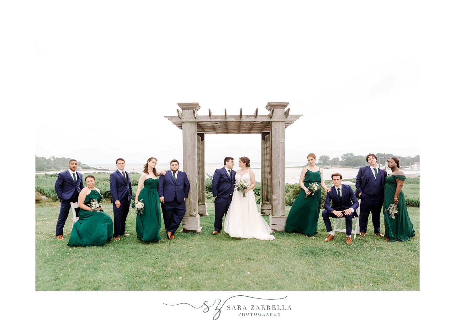 bride and groom stand with wedding party near stone arbor in front of Narragansett Bay