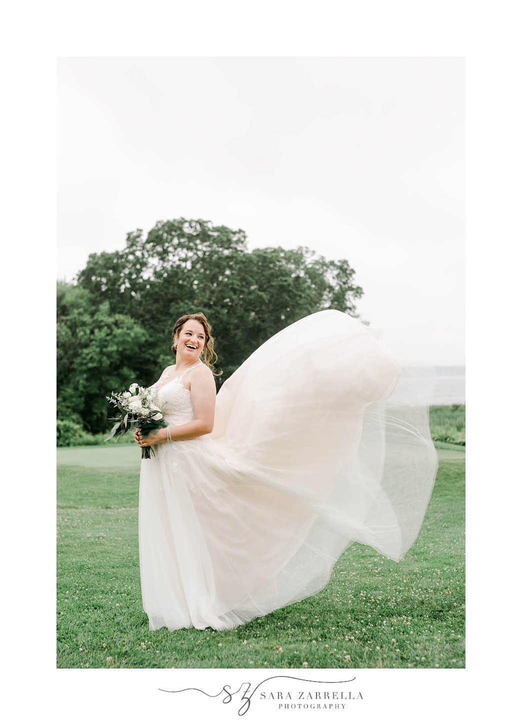 bride smiles while wedding dress skirt floats behind her on hill at Harbor Lights 