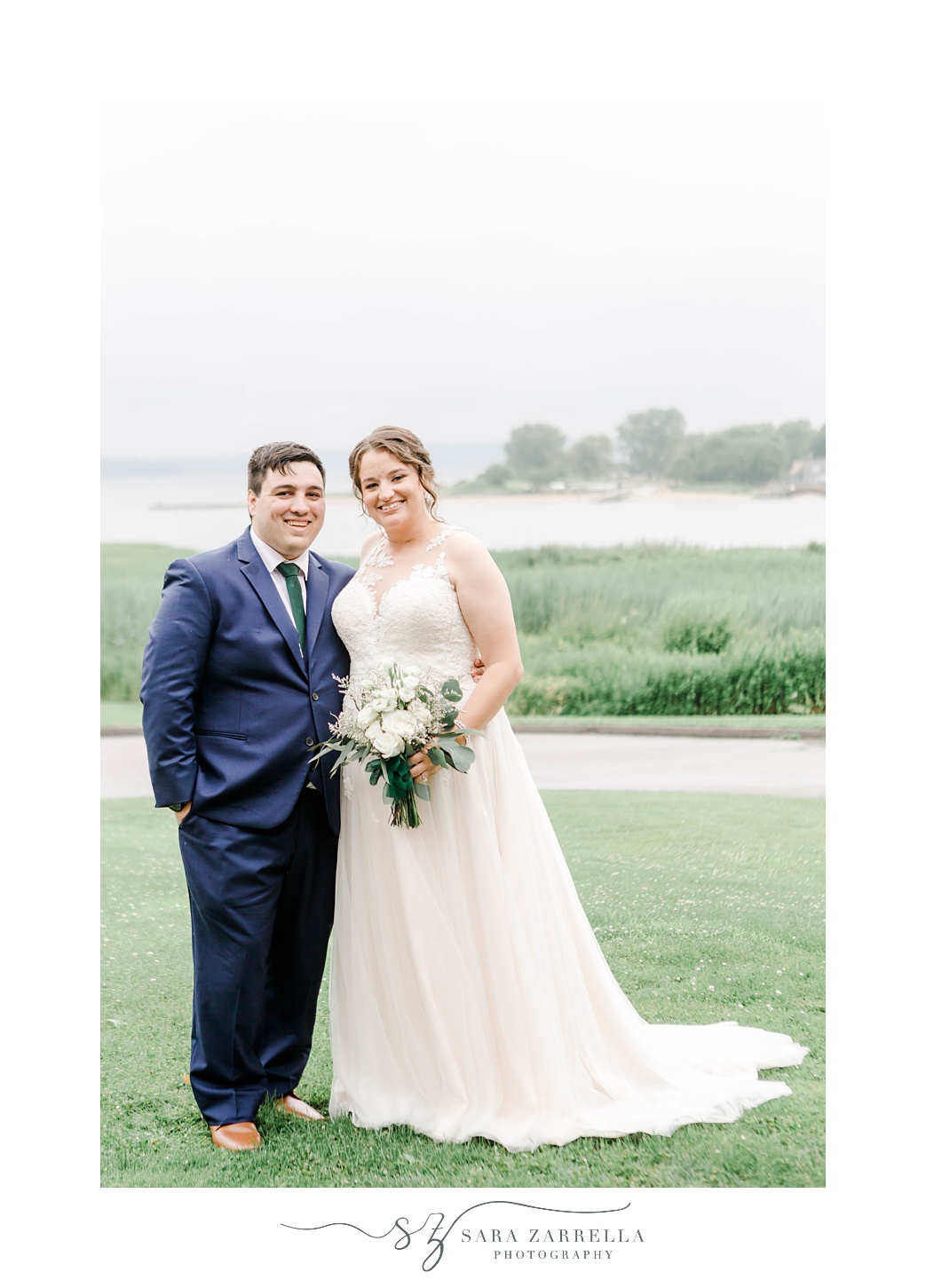 bride and groom hug on hill in front of Narragansett Bay at Harbor Lights 