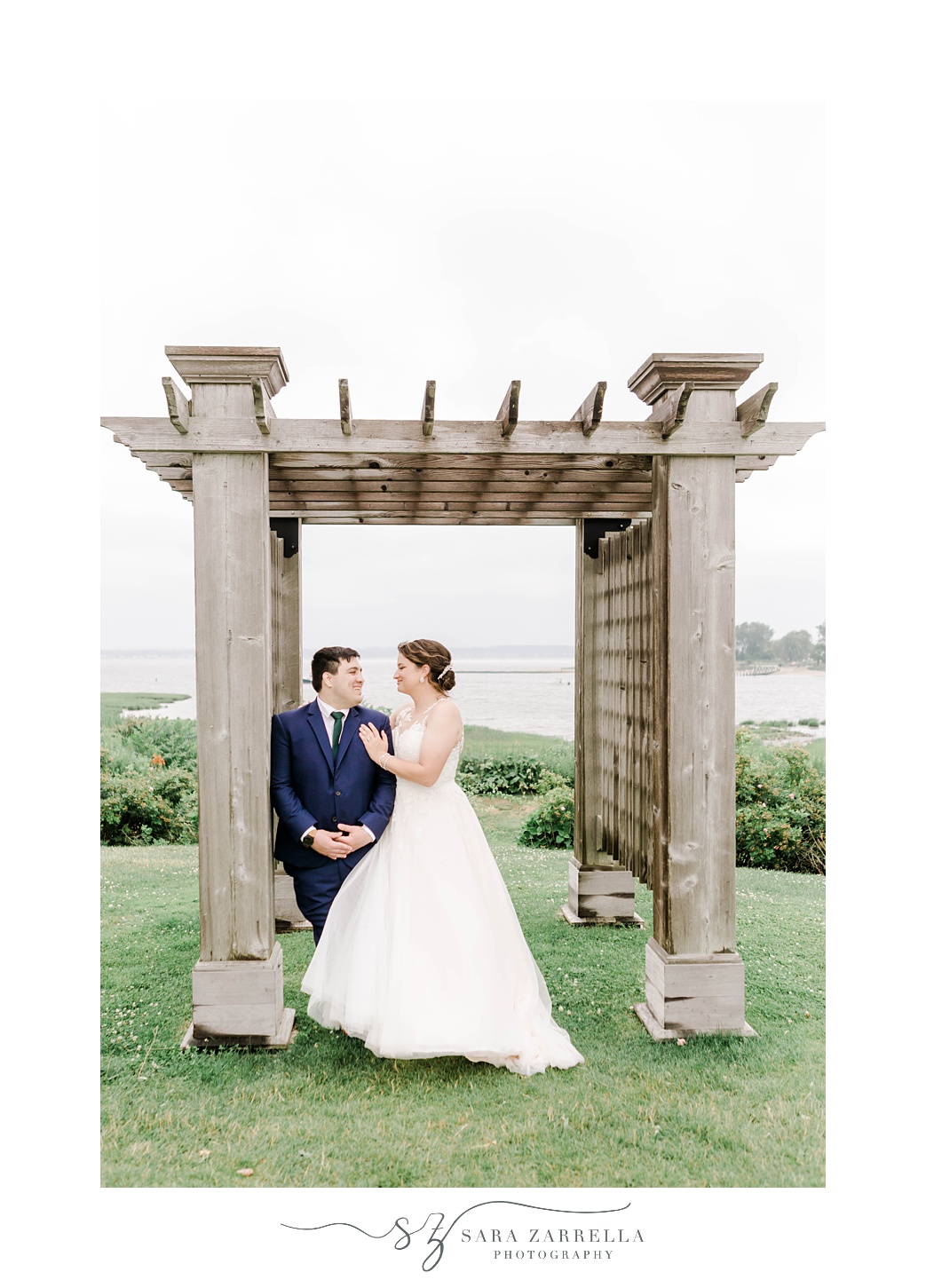 bride smiles at groom with both of them leaning on arbor at Harbor Lights 