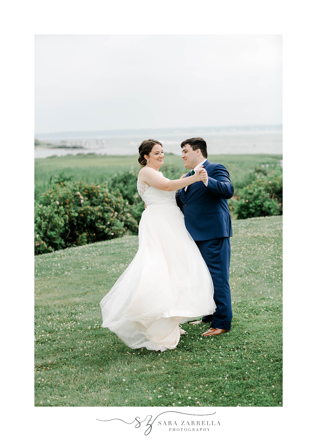 groom starts to dip bride on hill in front of Narragansett Bay