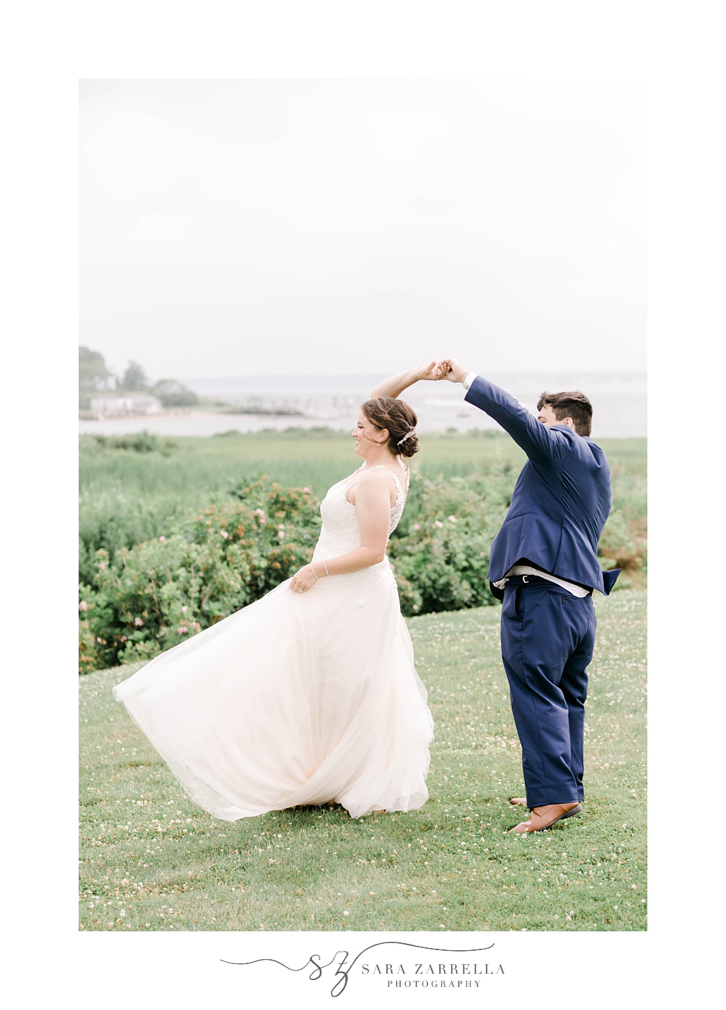 groom in navy suit twirls bride on hill at Harbor Lights 