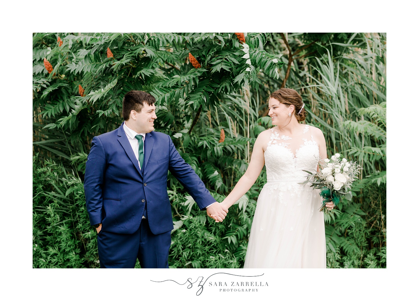 bride and groom hold hands in front of green trees in Warwick, RI